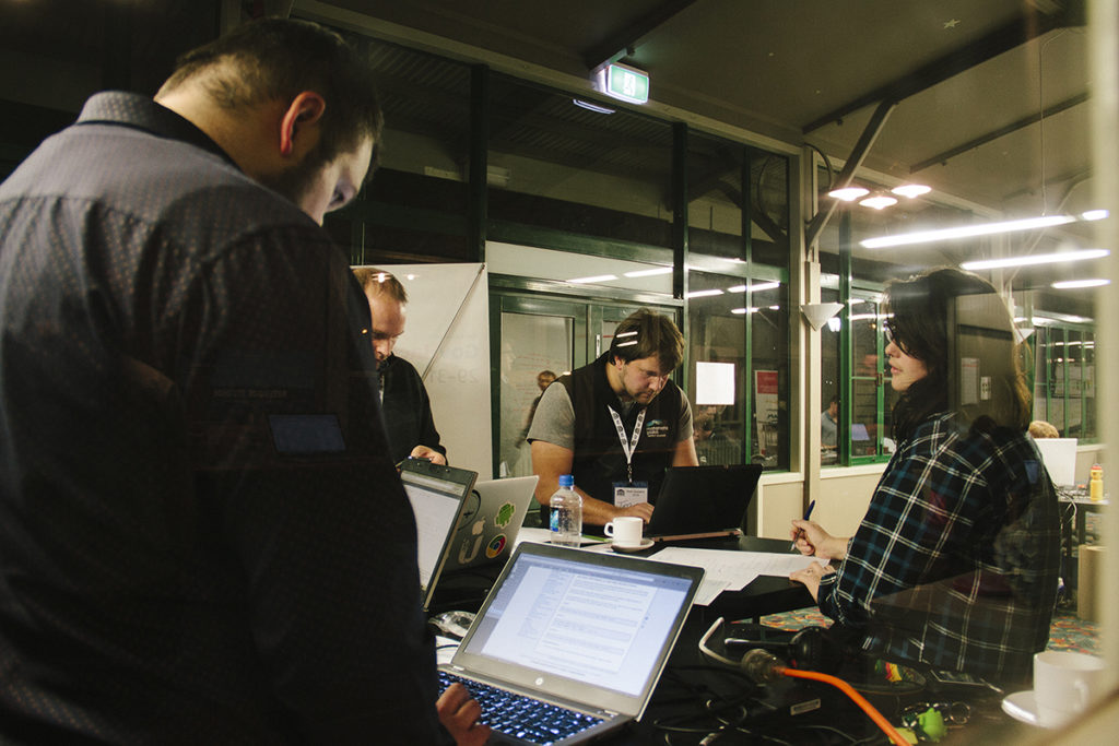 A group of young people, all crowded around laptops on a desk, their heads down working